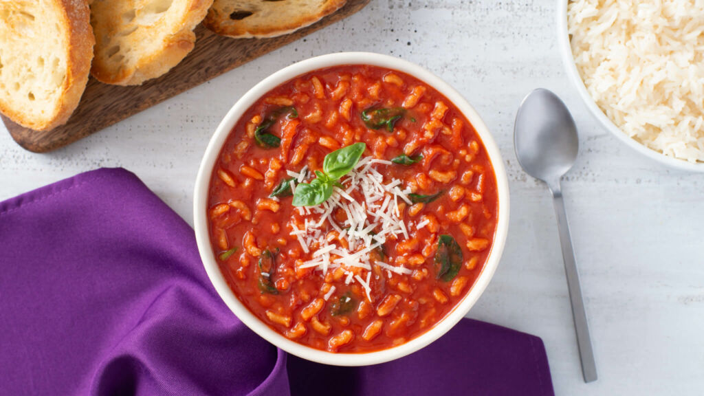 White bowl with tomato rice soup topped with cheese, and toasted bread