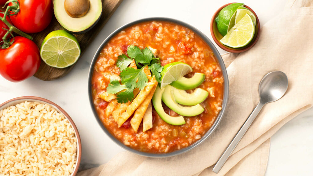 Bowl of tortilla rice soup topped with avocado, cilantro and lime slices