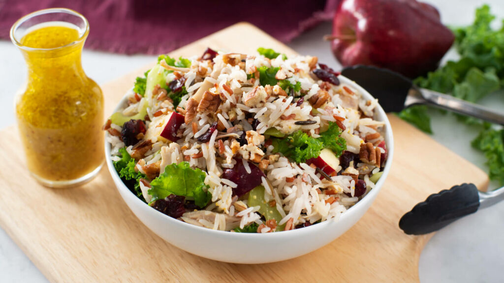 Salad bowl with rice, kale, chicken and a bottle of orange dressing